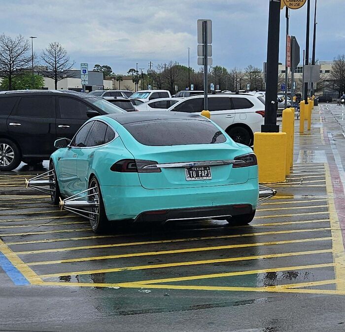 Teal car parked wrongly across multiple spots in a rainy parking lot.