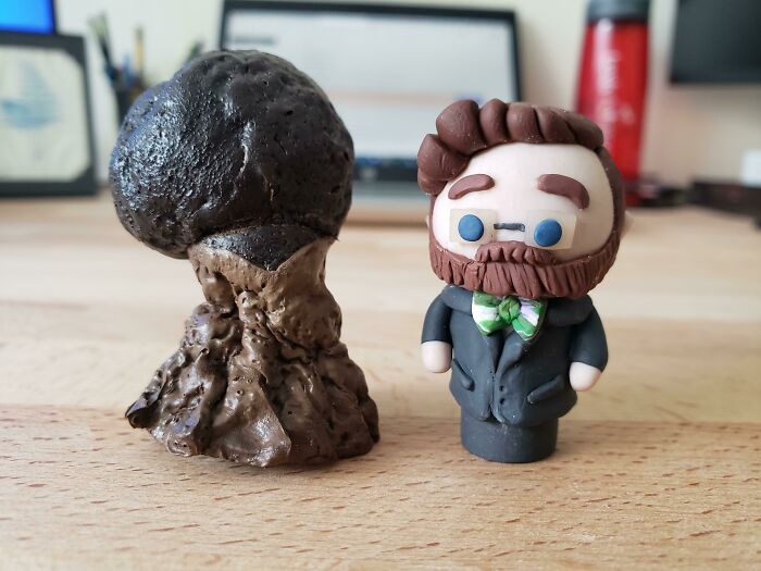 Clay figure resembling a man beside a burnt, deformed clay structure on a wooden table.