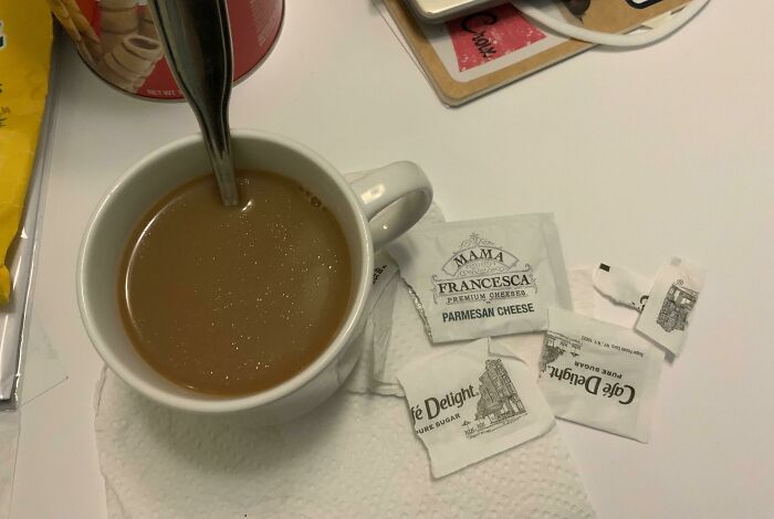 Cup of coffee with Parmesan cheese packets mistakenly used instead of sugar, showcasing a bad day mishap.