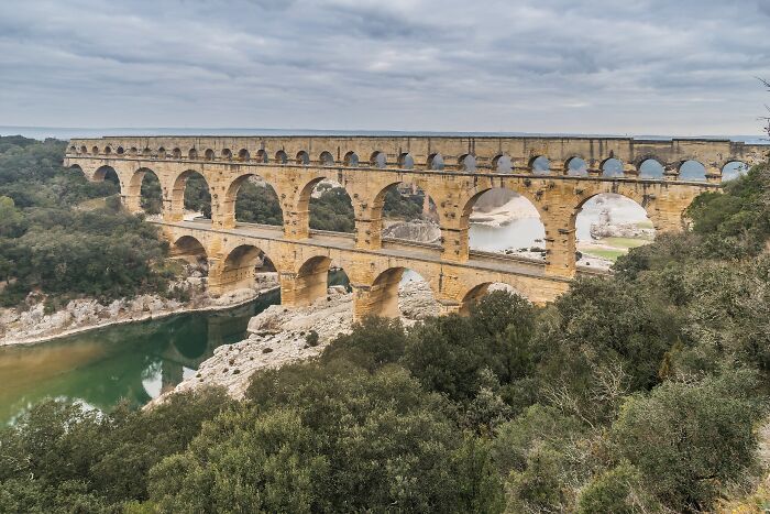 Ancient architectural wonder with stone arches spanning a river landscape under a cloudy sky. Ancient architectural wonder with stone arches spanning a river landscape under a cloudy sky.
