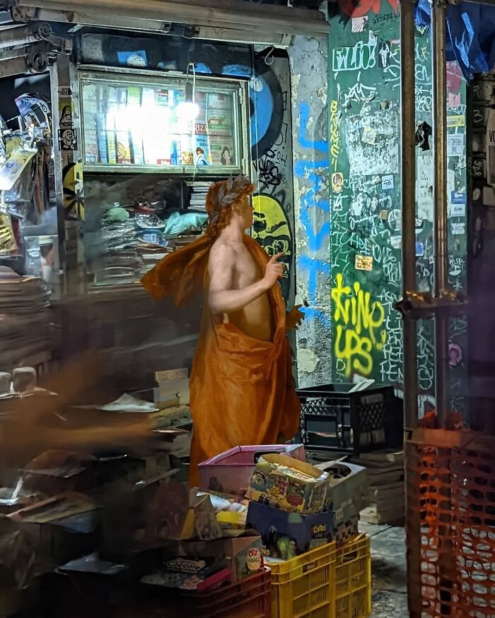 Classical figure in a modern urban setting by Alexey Kondakov, standing near a graffiti-covered wall and market stall.