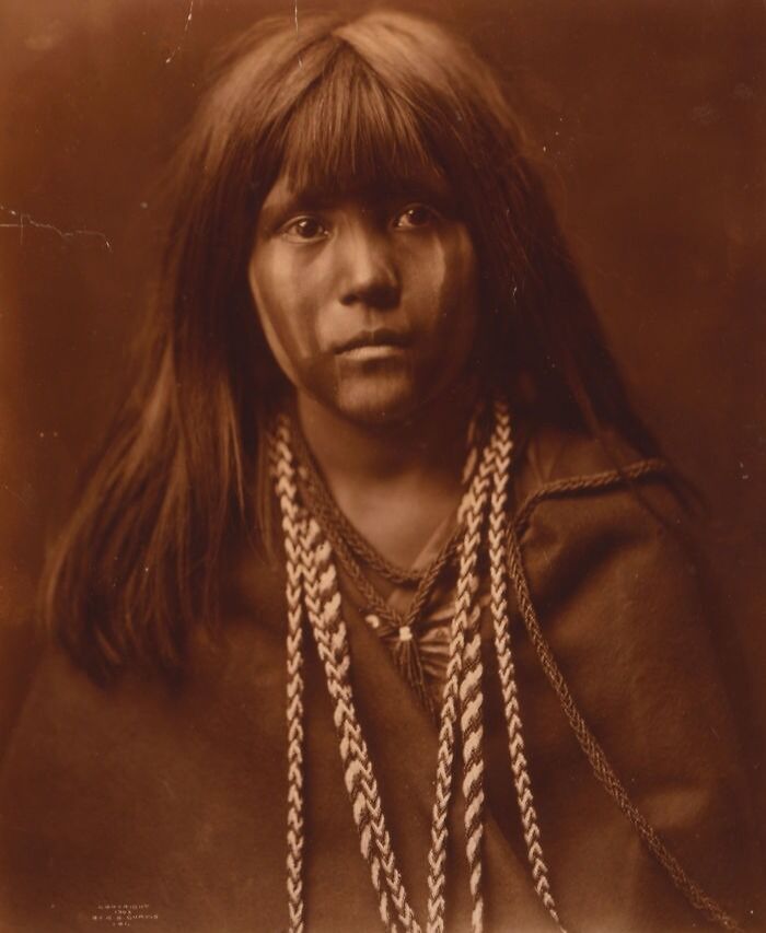 Native American woman with traditional face paint and braided hair, captured in a haunting historic portrait.