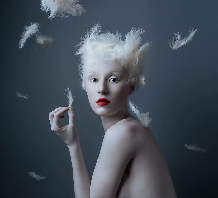 Surreal self-portrait of an artist with white feathers in hair, using Photoshop for dreamlike effects.