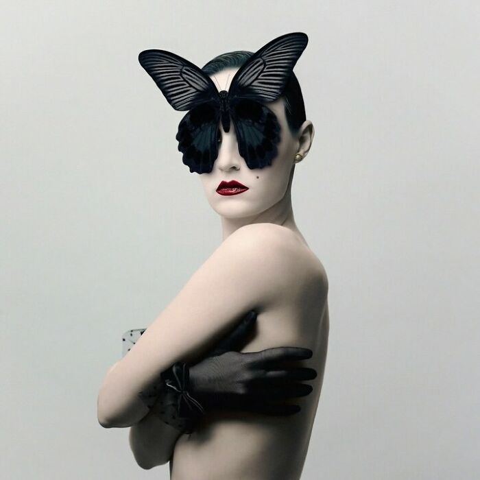 Surreal self-portrait of a woman with butterfly glasses, red lipstick, and wearing black gloves.
