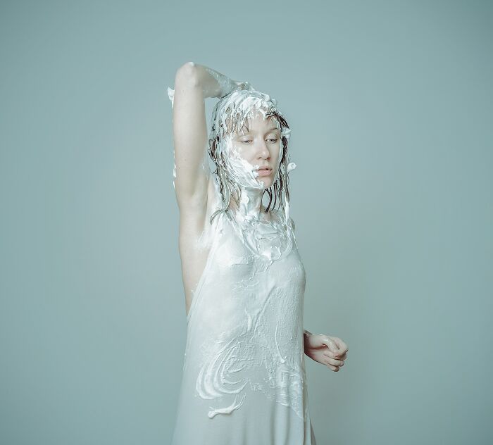Artist in surreal self-portrait, covered in white cream against a muted background, embodying dreamlike imagery.