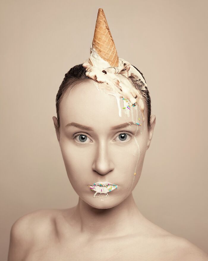 Surreal self-portrait of an artist with an ice cream cone on her head and sprinkles on her lips.