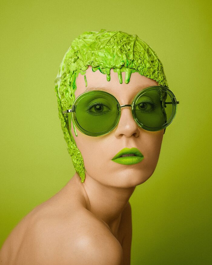 Surreal self-portrait featuring a woman with green glasses and vibrant makeup against a matching green background.