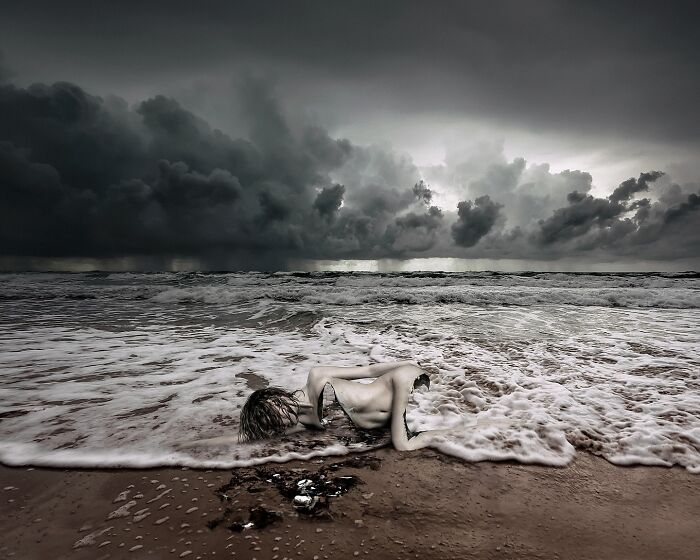 Surreal self-portrait of a woman lying on a stormy beach with dark clouds overhead, blending dream and reality through Photoshop.