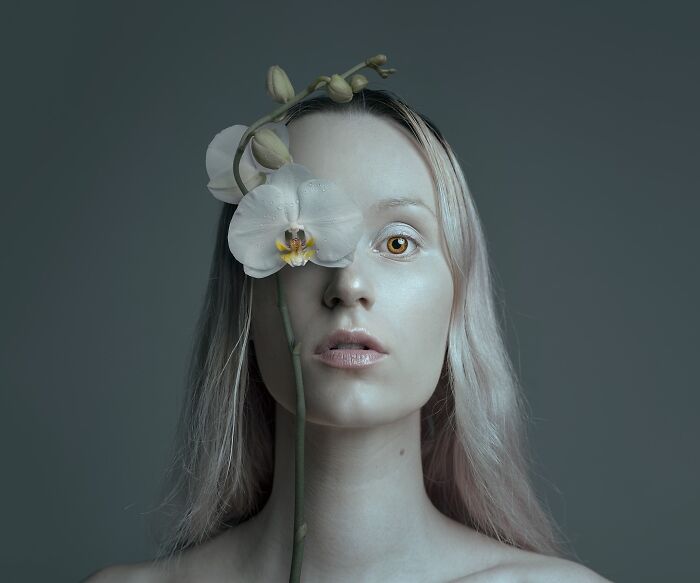 A surreal self-portrait of an artist with a white orchid covering one eye, blending reality and dreamlike elements.