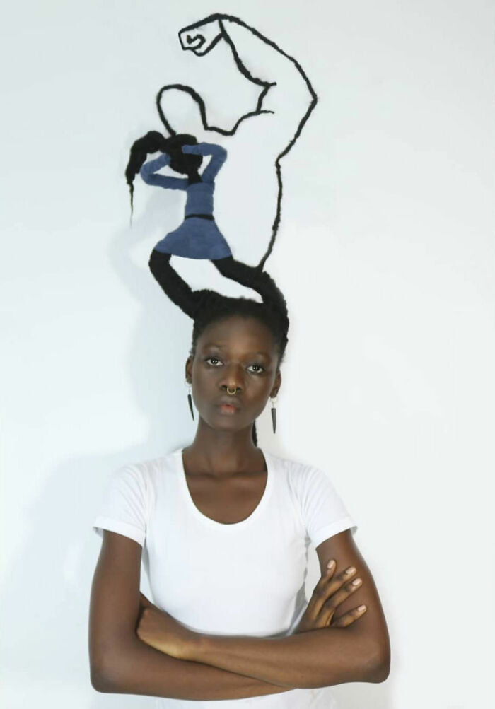 Artist with a hair sculpture shaped like a flexing arm, wearing a white shirt and earrings.