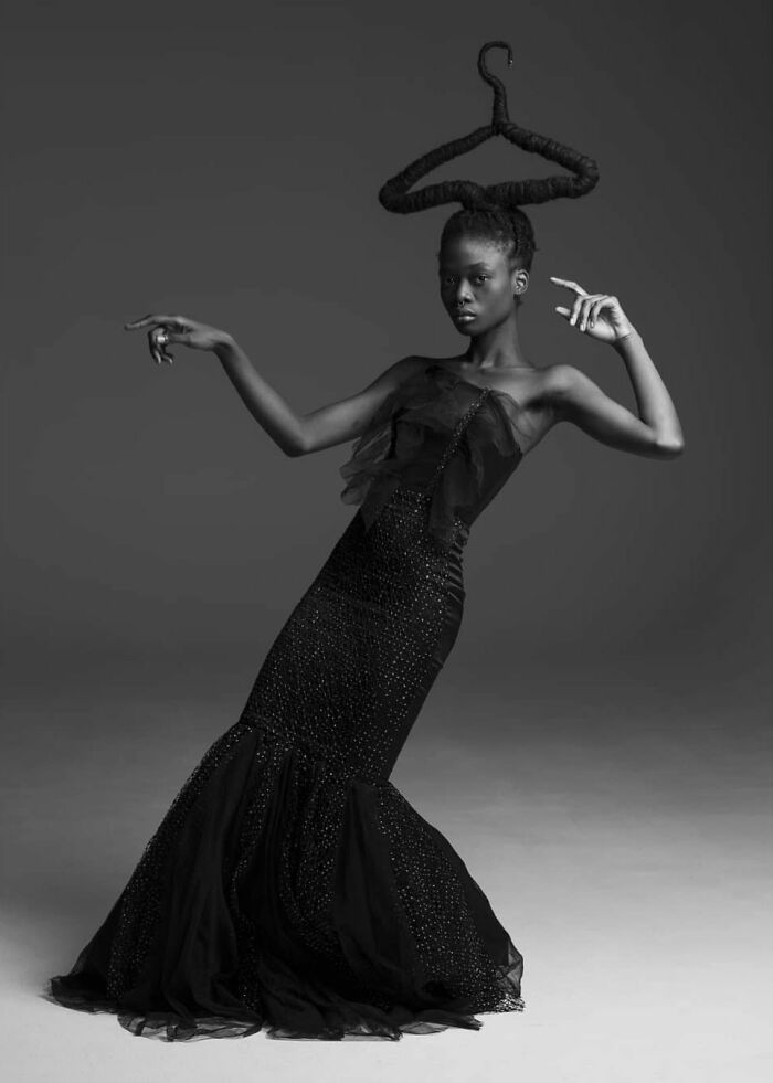 Woman posing with sculpted hair, wearing an elegant black gown in a studio.