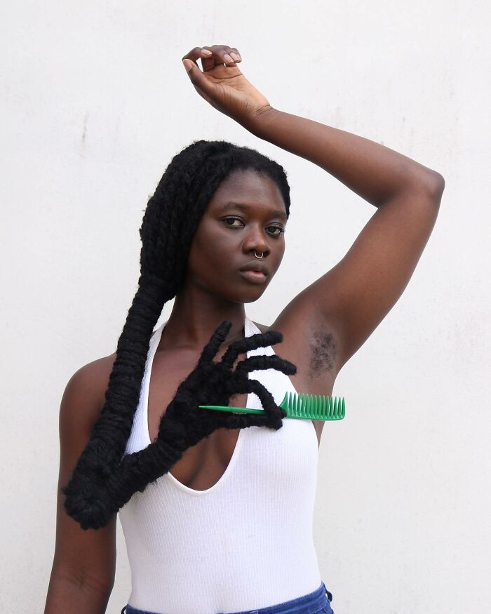 Artist with hair sculpted into hand shape holding a green comb.