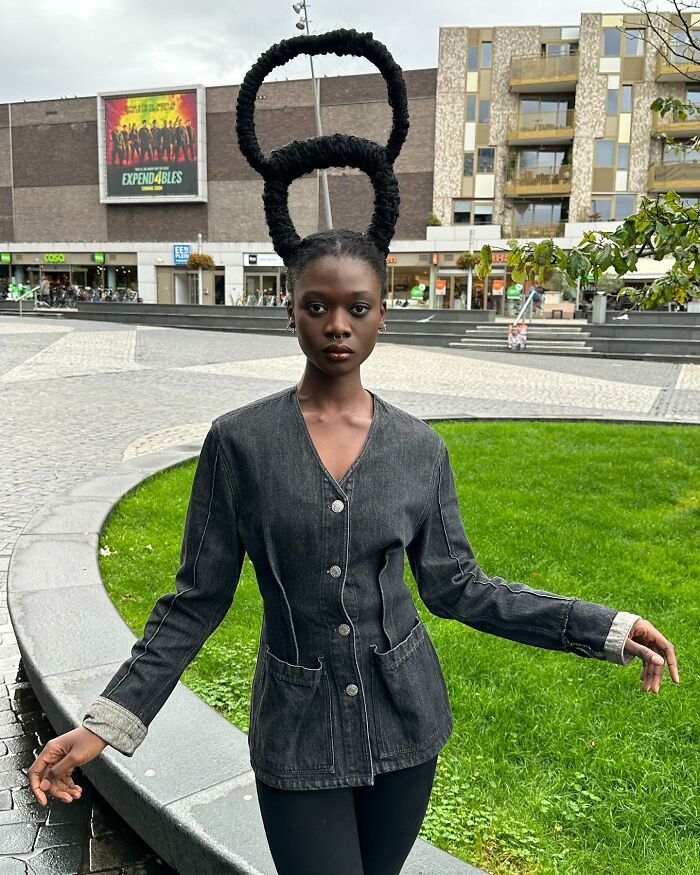 Woman showcasing incredible hair sculpture in urban setting, wearing a denim jacket.