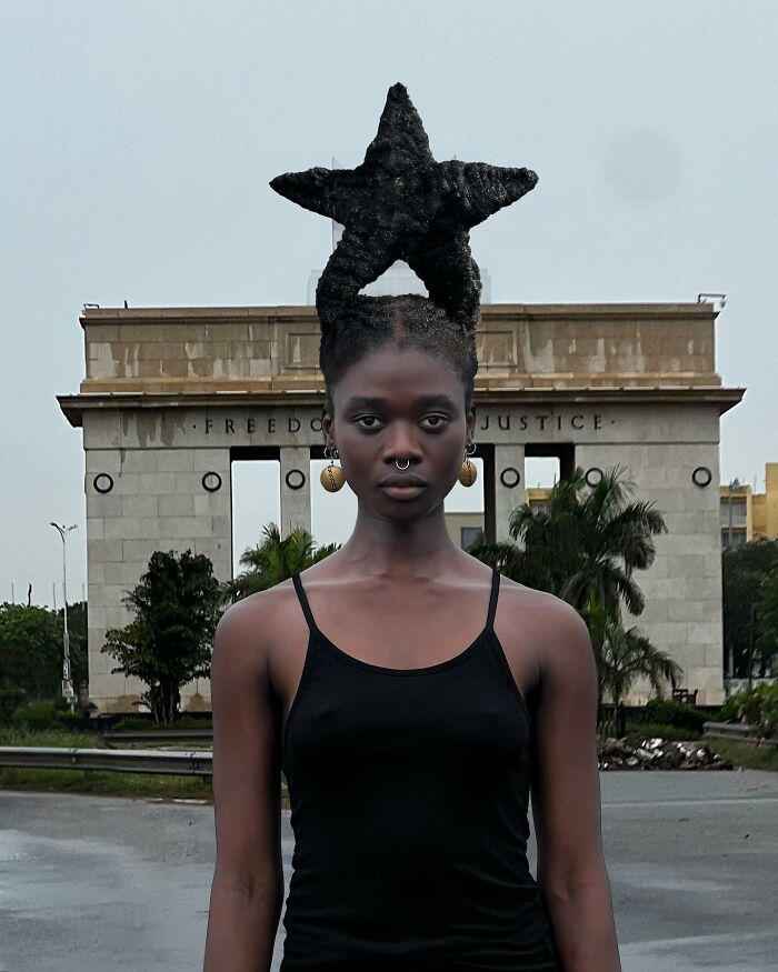 Woman with star-shaped hair sculpture poses in front of monument.