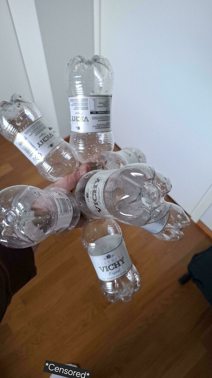 Hand holding six empty Vichy water bottles arranged to look like a bouquet in a wooden floor room unremarkable photos.