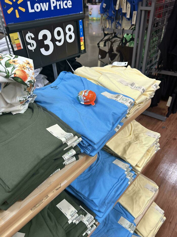 Stack of plain T-shirts in green, blue, and yellow priced at $3.98 with a Kinder Surprise toy on display, an unremarkable photo.