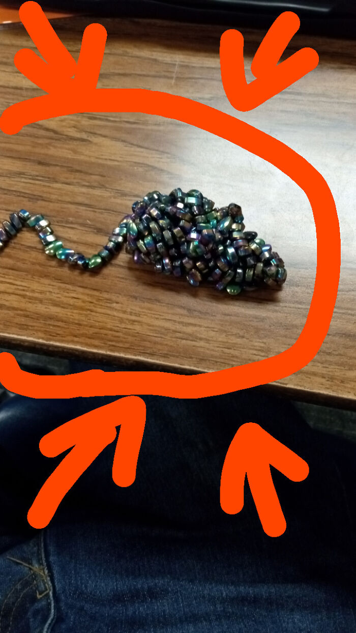 Unremarkable photo of a beaded object shaped like a mouse on a wooden surface with orange markings.
