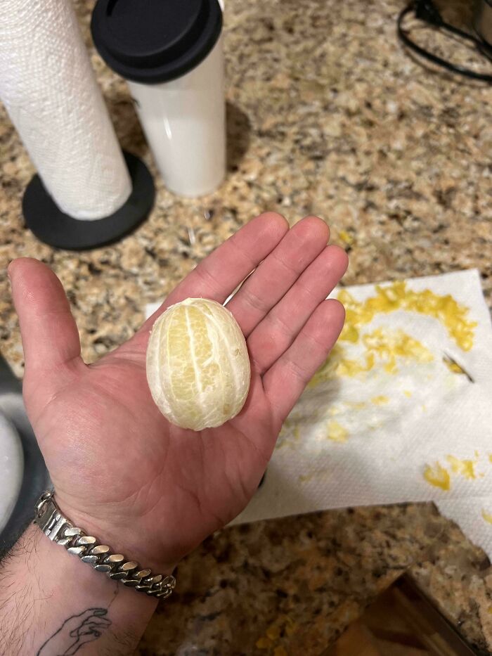 Hand holding a peeled lemon on a kitchen counter with paper towels and cup, showcasing an unremarkable photo entertaining moment.