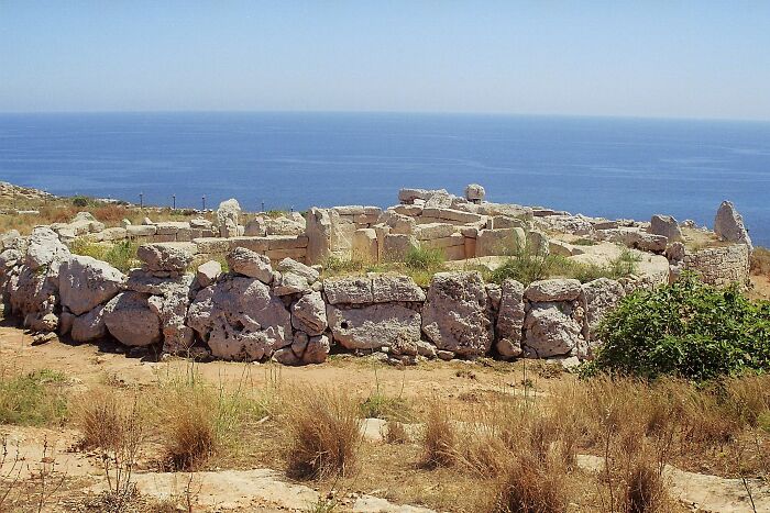 Ancient man-made stone structure on a coastal landscape with the sea in the background under a clear sky.