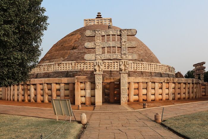 Ancient man-made structure with intricate stone carvings and a large dome under a clear sky.