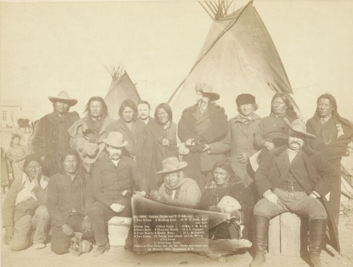 Group of cowboys and Native Americans gathered near tipis in an authentic 1800s historical photo.