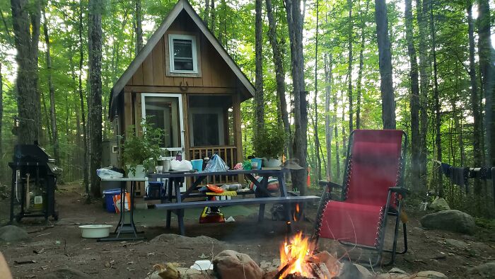 A clever tiny home with a picnic table and campfire surrounded by trees, inspiring life off the grid.