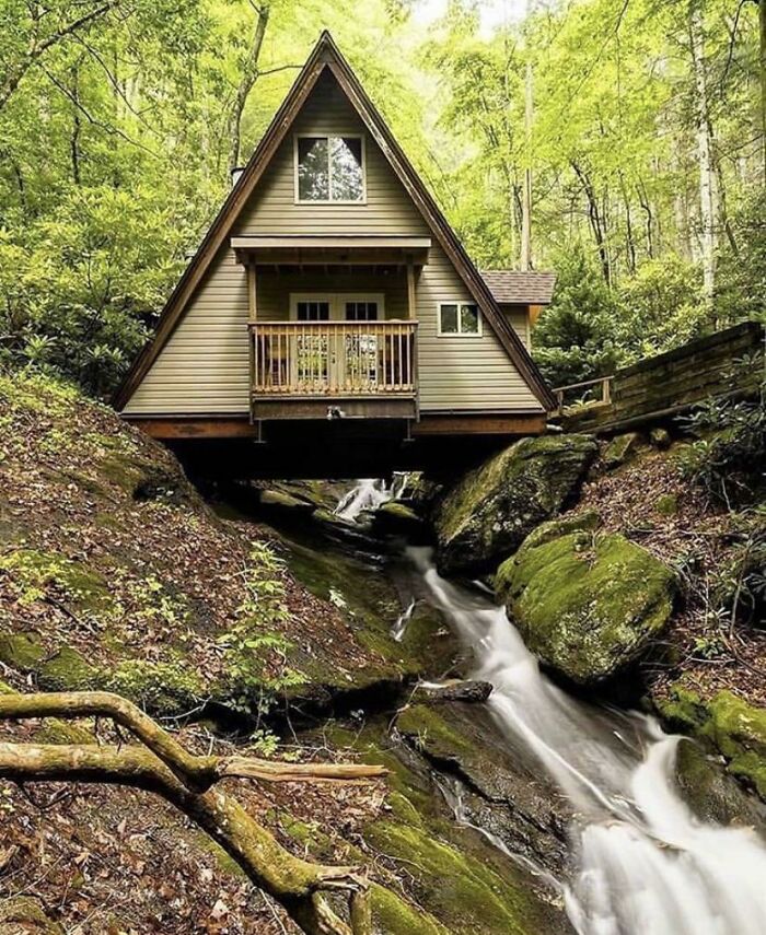 A unique tiny home with an A-frame design elevated over a forest stream, inspiring off the grid living.