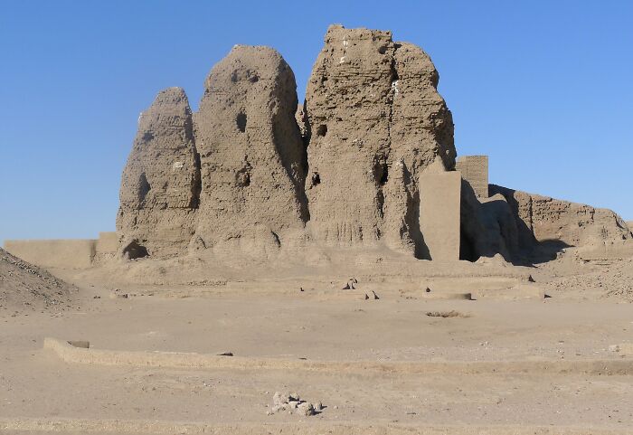 Ancient man-made mud-brick structure standing in a desert landscape under a clear blue sky.