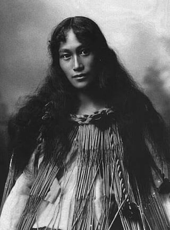 Native American woman with long hair wearing traditional attire in a haunting vintage photo from a century ago.