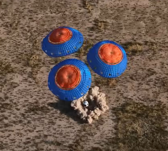 Parachutes with blue and orange canopies land a capsule on a dry, grassy area, related to Blue Origin flight. Parachutes with blue and orange canopies land a capsule on a dry, grassy area, related to Blue Origin flight.