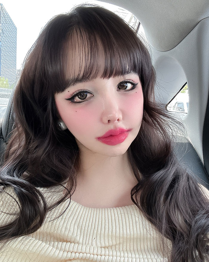 K-Pop star posing in a car, with long hair and glamorous makeup highlighting drastic transformation. K-Pop star posing in a car, with long hair and glamorous makeup highlighting drastic transformation.