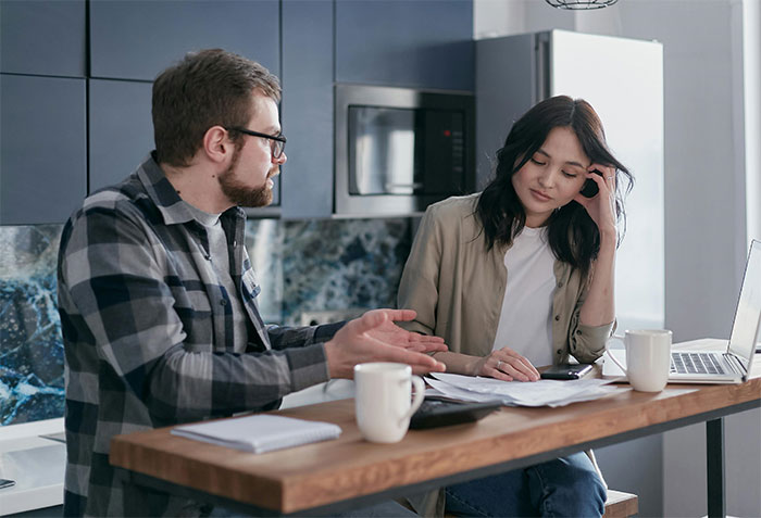 Couple discussing lottery winnings at kitchen table, appearing thoughtful and serious. Couple discussing lottery winnings at kitchen table, appearing thoughtful and serious.