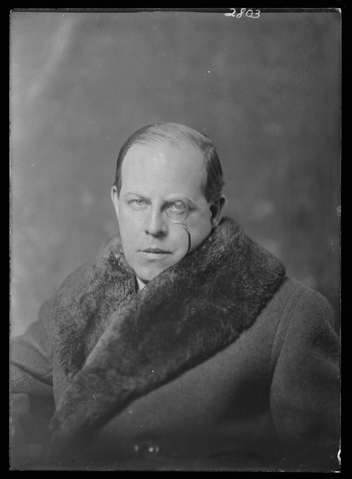 Black and white rare photograph of a man wearing a fur-collared coat and monocle, restored from glass negatives.