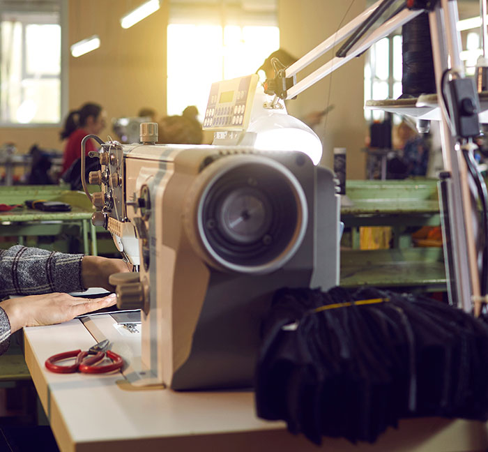 Worker sewing fabric on machine in factory, illustrating impact of US tariffs. Worker sewing fabric on machine in factory, illustrating impact of US tariffs.
