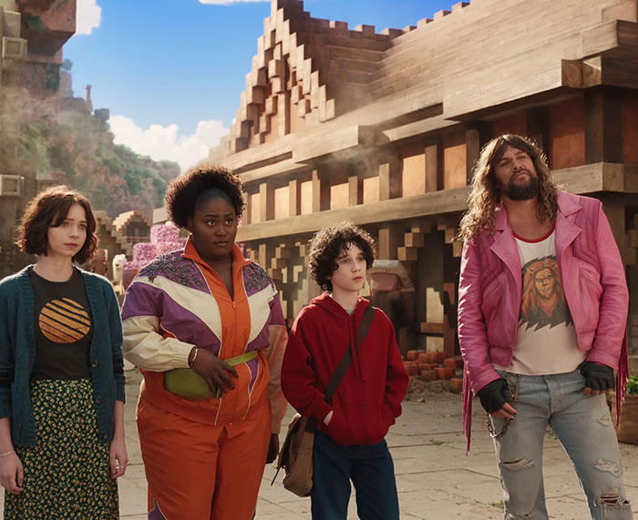 Four people standing in a 'Minecraft' scene with wooden buildings, one in a pink jacket and jeans. Four people standing in a 'Minecraft' scene with wooden buildings, one in a pink jacket and jeans.