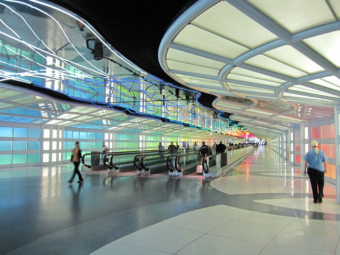 Passengers walking through a colorful airport terminal with moving walkways. Passengers walking through a colorful airport terminal with moving walkways.