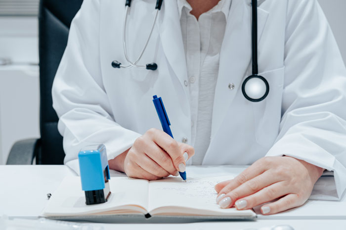 Doctor writing in a notebook, wearing a white coat and stethoscope, symbolizing appointment scheduling. Doctor writing in a notebook, wearing a white coat and stethoscope, symbolizing appointment scheduling.