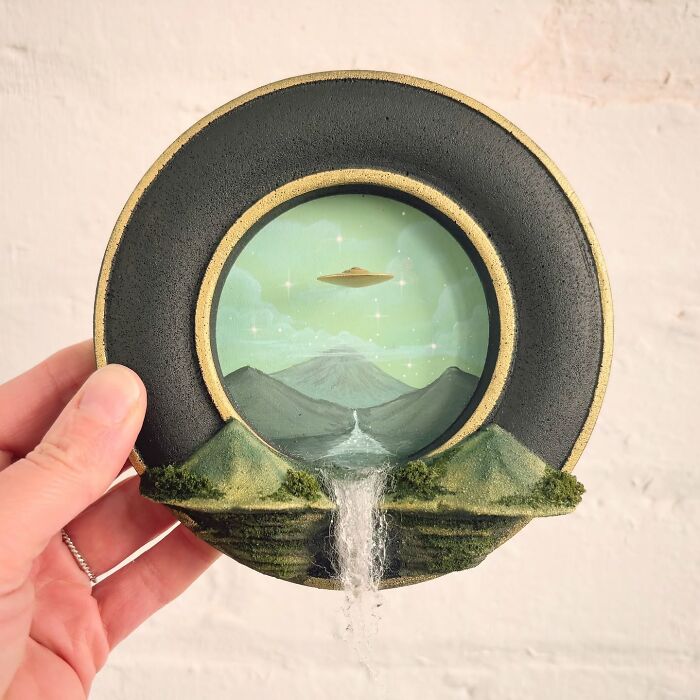 Hand holding a mysterious diorama featuring a UFO over mountains with a waterfall, perfect for alien enthusiasts.