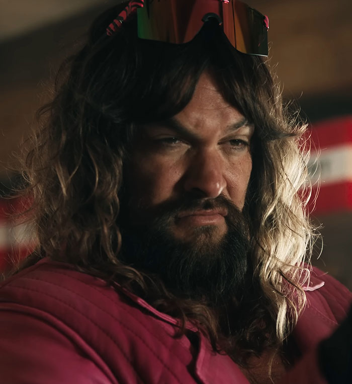 A man with long hair and sunglasses, wearing a pink shirt in a dimly lit room. A man with long hair and sunglasses, wearing a pink shirt in a dimly lit room.