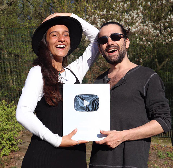 Two smiling people outdoors holding a YouTube award, highlighting a mysterious illness while traveling. Two smiling people outdoors holding a YouTube award, highlighting a mysterious illness while traveling.