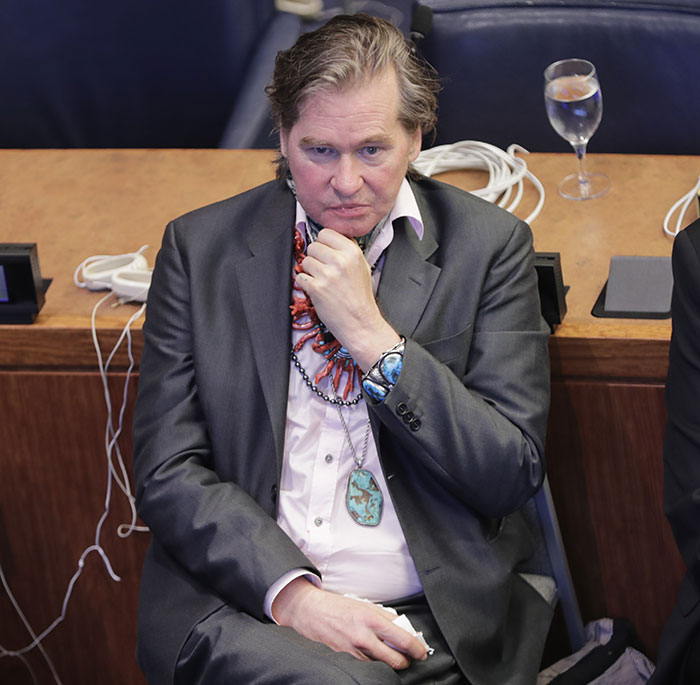 Legendary actor Val Kilmer seated in a suit, wearing a turquoise necklace and bracelet at an event. Legendary actor Val Kilmer seated in a suit, wearing a turquoise necklace and bracelet at an event.