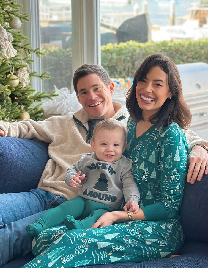 A family sitting on a couch, smiling, near a festive tree; associated with 'Pitch Perfect' actor news. A family sitting on a couch, smiling, near a festive tree; associated with 'Pitch Perfect' actor news.