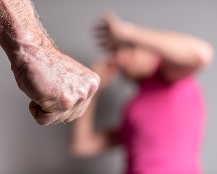A man's clenched fist in focus, blurred woman in pink shirt shields herself, illustrating forceful confrontation. A man's clenched fist in focus, blurred woman in pink shirt shields herself, illustrating forceful confrontation.