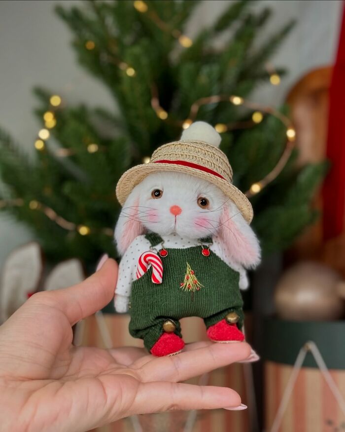 Handmade whimsical plush toy rabbit in festive attire, held in front of a Christmas tree.