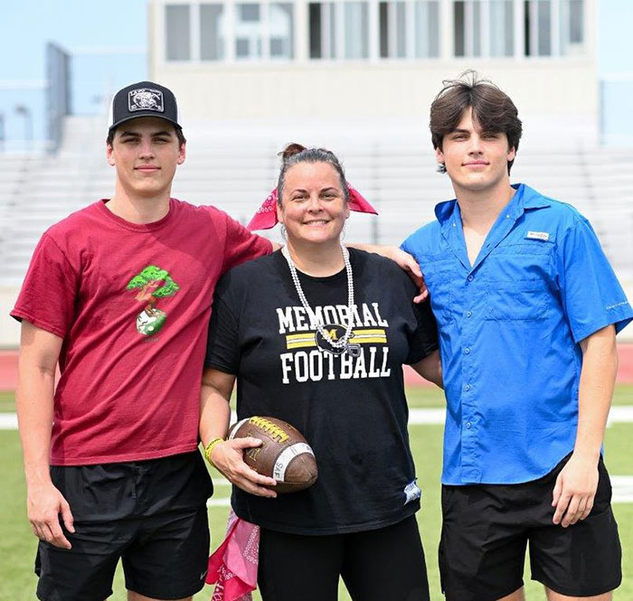 Two brothers and a woman stand on a sports field, one wearing a "Memorial Football" shirt. Two brothers and a woman stand on a sports field, one wearing a "Memorial Football" shirt.
