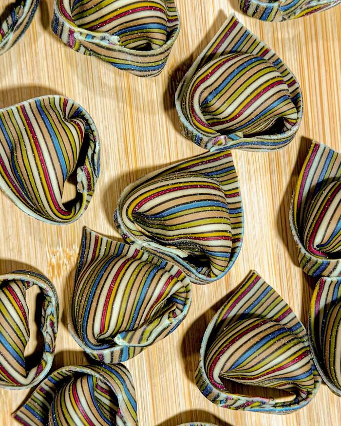 Colorful handcrafted pasta with striped patterns on a wooden surface.