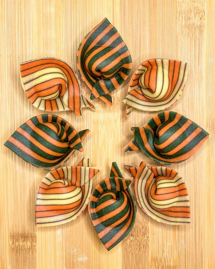 Colorful handcrafted pasta with orange, green, and cream stripes, arranged in a circular pattern on a wooden surface.