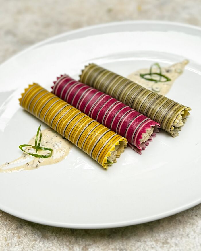 Colorful handcrafted pasta rolls on a white plate, featuring intricate striped patterns in yellow, red, and green.