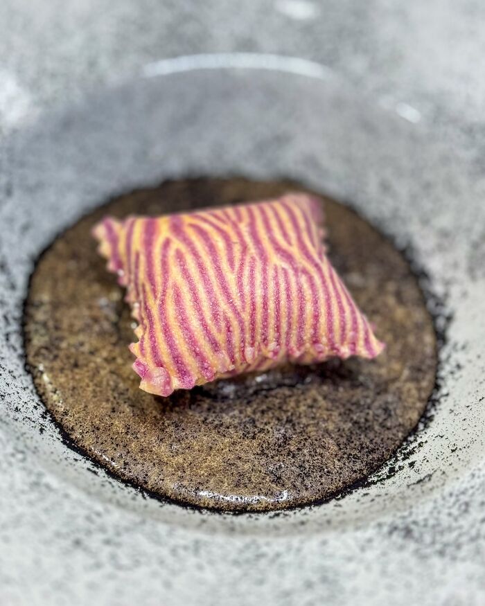 Handcrafted pasta with vibrant pink and yellow stripes on a textured plate.