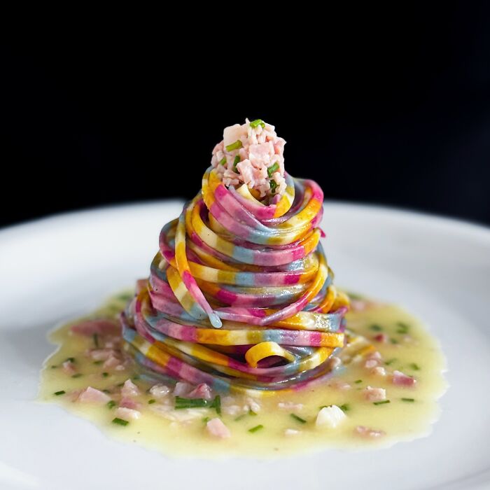 Colorful handcrafted pasta with vibrant patterns, crafted by a culinary artist, elegantly plated with a creamy sauce.
